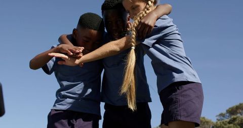 Teen students embracing on school playground in light blue shirts and navy shorts