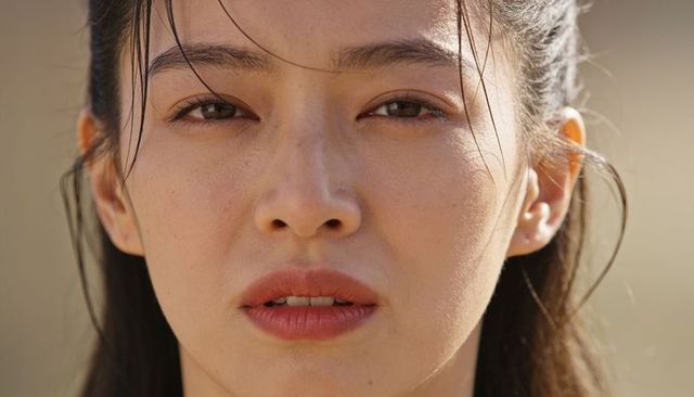 Gazing asian woman close-up showing natural skin texture, loose hair strands, earlobe stud