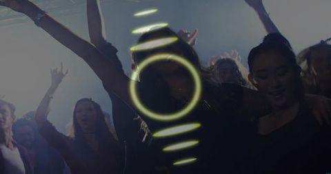 Nightclub crowd dancing under neon ring lighting, energetic female raising arms