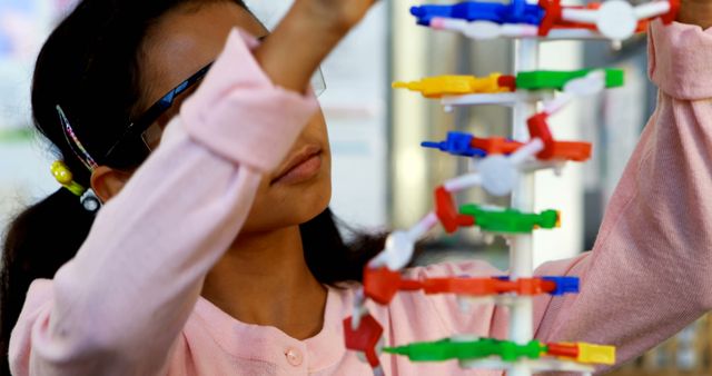 A young Asian girl is focused on examining a DNA model, with copy space. Her interest in science is evident as she engages with the educational tool.