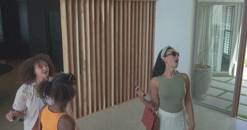 African american women friends reacting to smartphone while entering modern daylight lobby