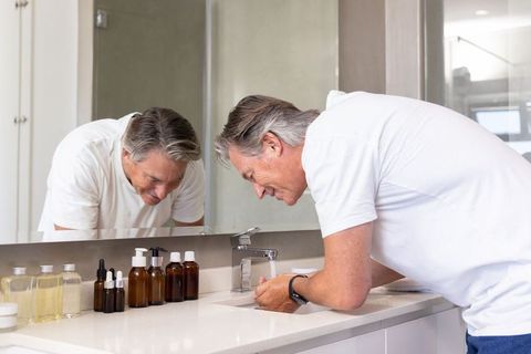 Mature man washing hands at modern bathroom vanity with chrome faucet and amber bottles
