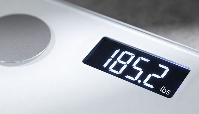 Glass digital bathroom scale displaying 185.2 lbs minimalist sleek chrome sensor