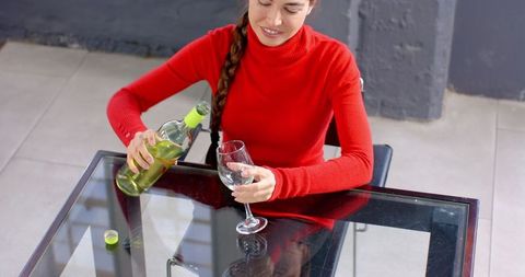 Woman in red sweater pouring white wine at office desk