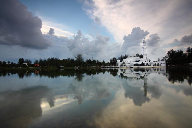 Beautiful image of a mosque reflected in a calm lake during sunset with dramatic clouds. Great for travel advertisements, religious blogs, architectural studies, and serene landscape backgrounds.