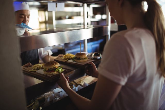 Chef passing tray with french fries and burger to waitress in the commercial kitchen