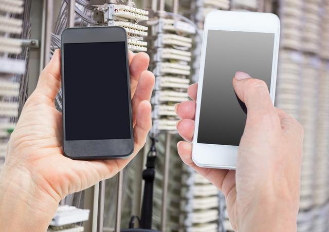 This image shows hands holding two mobile phones in a server room, highlighting the connection between mobile technology and data infrastructure. Ideal for use in articles or advertisements related to IT services, telecommunications, data management, and mobile technology.