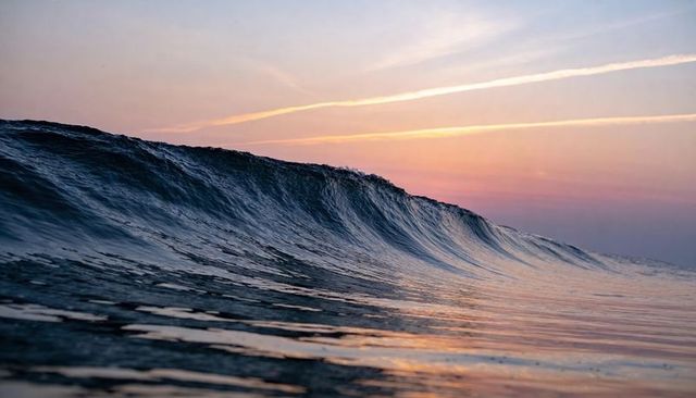 Glassy ocean wave curling at pastel sunrise with contrails, rolling swell, textured crest