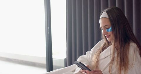 Woman in towel reviewing smartphone for self-care routine