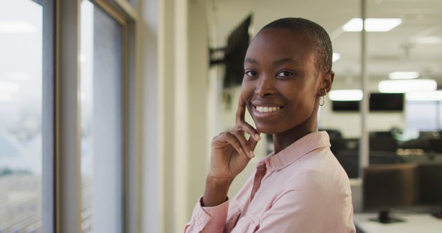 A smiling, confident Black businesswoman standing by a window in a modern office. Suitable for business, corporate, and professional themes. Ideal for advertisements, websites, presentations, or articles focusing on entrepreneurship, workspace inspiration, and career success.