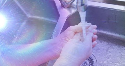 Senior woman's hands under flowing water with rainbow light