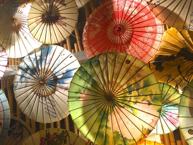 Beautifully crafted traditional Asian umbrellas showcased in ceiling display, perfect for use in articles or posts related to Asian cultures, traditional arts, decor ideas, and cultural exhibitions. Excellent for travel blogs, cultural reports, and artistic projects to highlight the intricate craftsmanship and vibrant colors of Asian decorations.