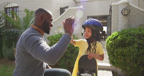 Father High-Fiving Daughter with Skateboard in Sunny Park