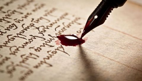 Fountain pen nib creating dark red ink droplet on vintage parchment macro close-up