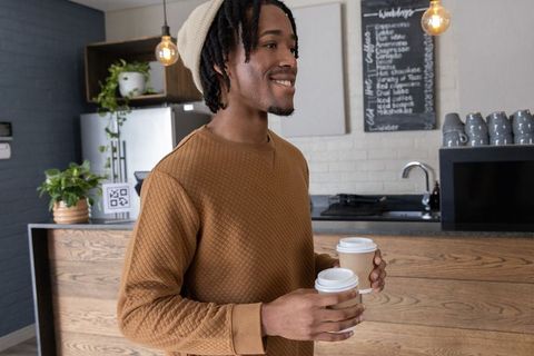 Smiling african american man holding two takeaway coffees at cozy modern cafe counter