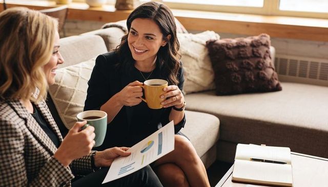 Women professionals discussing charts over coffee in cozy office lounge for teamwork