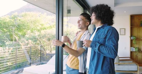 Smiling Friends Enjoying View Through Glass Door with Coffee Mugs