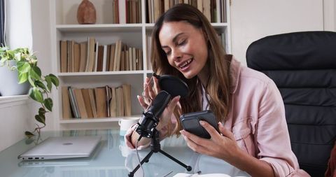 Woman podcasting in home office with microphone and smartphone