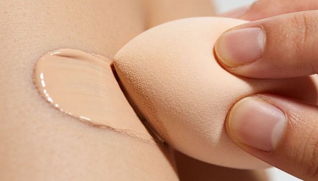 Blending liquid foundation with teardrop makeup sponge closeup on bare skin