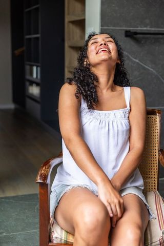 African american woman laughing and relaxing on cane armchair in cozy living room
