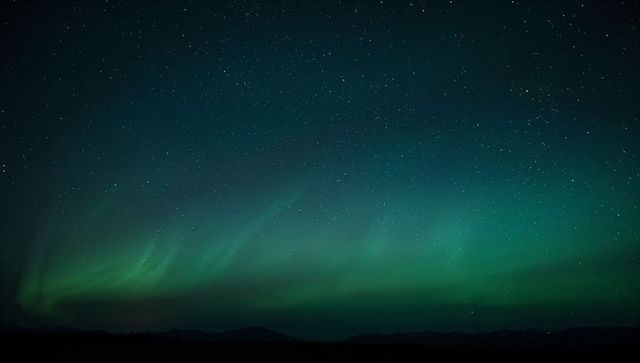 Dancing aurora borealis sweeping across starry northern sky over silhouetted mountains
