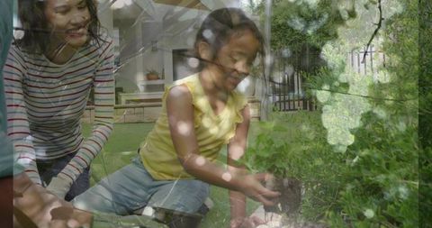 Mother guiding daughter planting seedling in backyard garden on sunny afternoon