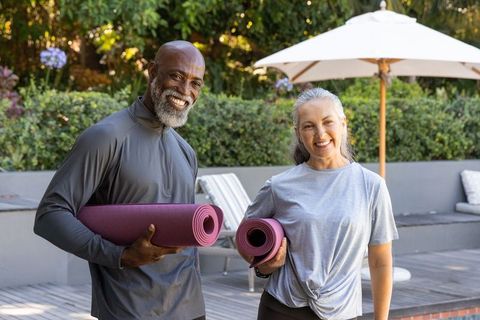 Sunlit senior couple carrying yoga mats on patio smiling after outdoor workout