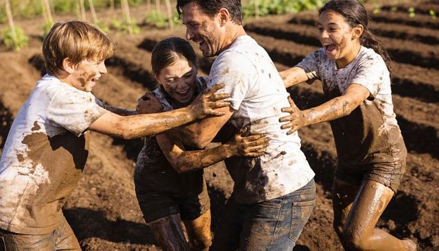 Outdoor mud play: dad and 3 kids laughing and bonding while splashing in garden furrows