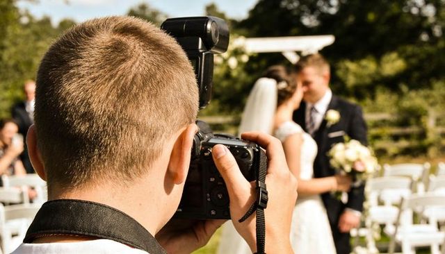 Wedding photographer capturing bride and groom embracing in sunlit garden ceremony