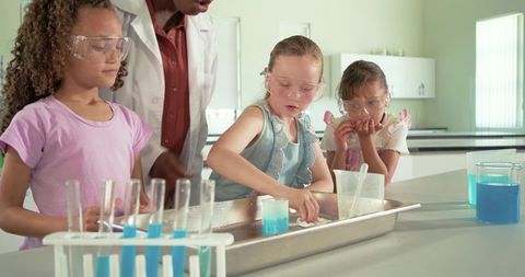 Diverse girls conducting hands-on blue chemistry experiment with african american teacher