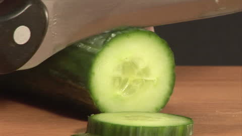 Close-up of Knife Slicing Fresh Cucumber on Cutting Board