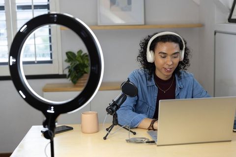 Nonbinary creator recording podcast with laptop, microphone and ring light in home studio
