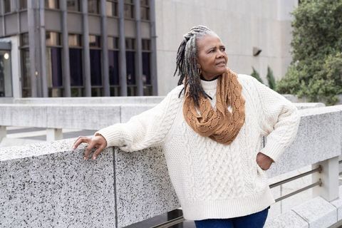 Senior african american woman leaning on urban concrete railing wearing cream cable-knit sweater