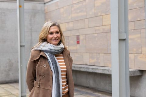 Smiling middle-aged woman wearing brown coat and gray scarf on urban walkway