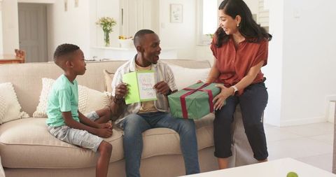 Family celebrating father's day at home, dad opening card and receiving gift on couch