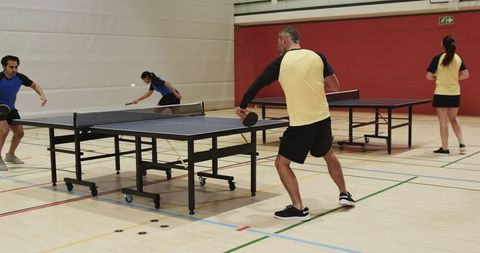 Adults Engaged in Competitive Table Tennis Doubles Match in Gymnasium