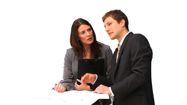 Two business professionals in formal attire engaged in discussion, with one holding a clipboard. Suitable for depicting corporate communication, team meetings, and strategic planning. Ideal for business-related presentations, websites, or corporate brochures highlighting professional teamwork and collaboration.