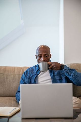 Man Drinking Coffee While Working on Laptop in Comfortable Living Room