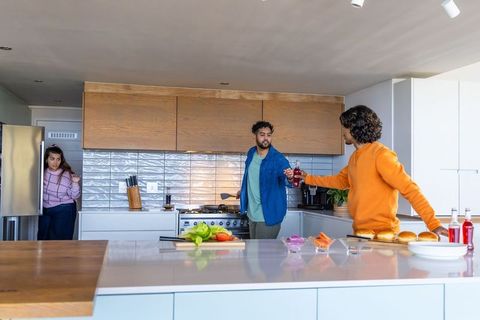 Multicultural friends preparing burgers and chatting at modern open-plan kitchen island