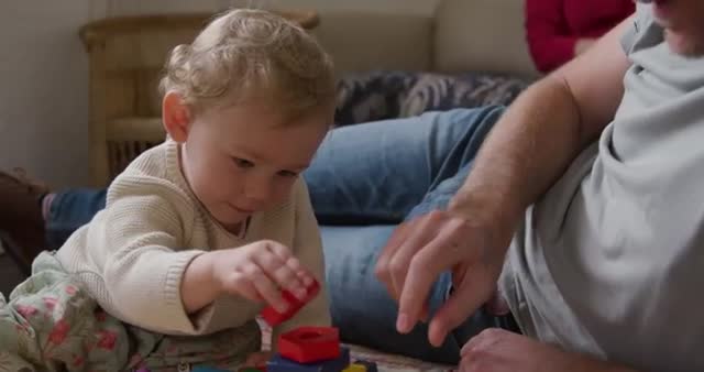 Father and baby enjoy bonding time at home, playing with colorful wooden blocks. The mother's presence in the background adds a sense of family unity and warmth. Perfect for themes related to family life, parenting activities, and early childhood development.