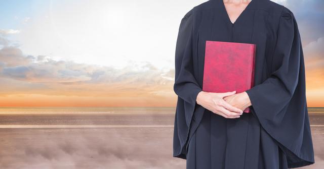 Judge holding red book with majestic sky and sunset in background. Evokes themes of justice, law, and authority. Useful for legal websites, law firm promotional materials, articles on judiciary, and blogs about legal topics.