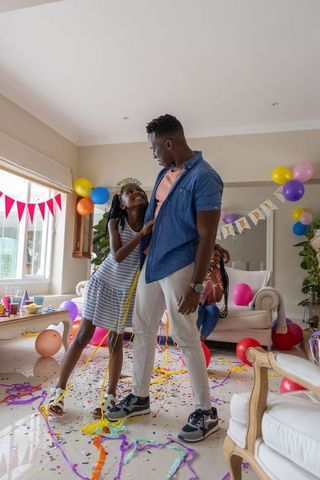 African american father daughter celebrating birthday at home with balloons confetti