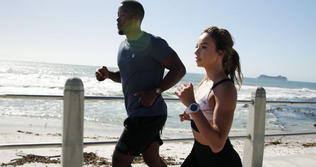 African American man and young biracial woman jogging by the sea. They're enjoying a sunny day of outdoor exercise with a scenic ocean backdrop.