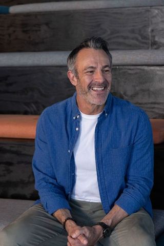 Middle-aged man smiling and relaxing on tiered bench in casual blue shirt