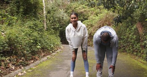Diverse couple taking break while jogging on mossy woodland trail during outdoor workout