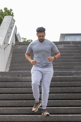 African american man running down urban concrete stairs wearing smartwatch and activewear