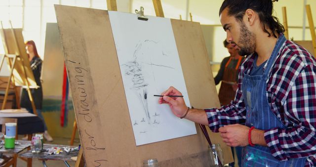 Young artist sketching on canvas in an art studio. Useful for highlighting creativity, art education, and the artistic process. Perfect for educational blogs, art tutorials, and promotional content for art classes or studios.