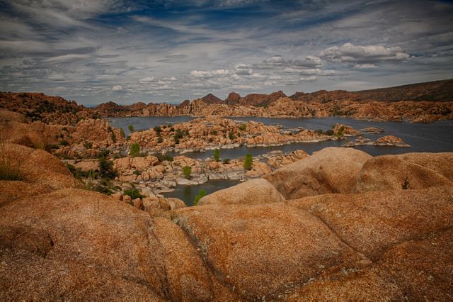 Image showcasing the stunning Granite Dells rock formations amid Watson Lake in Arizona under a partly cloudy sky. Ideal for travel magazines, tourism websites, outdoor adventure blogs, and nature documentaries highlighting scenic vistas and geological features.