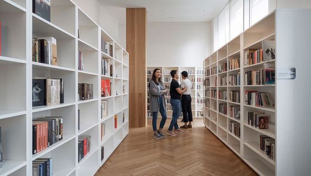 Trio browsing modern minimalist library with white shelves and herringbone wood floor