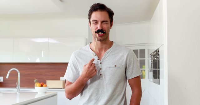 Handsome man with fake mustaches making faces in the kitchen